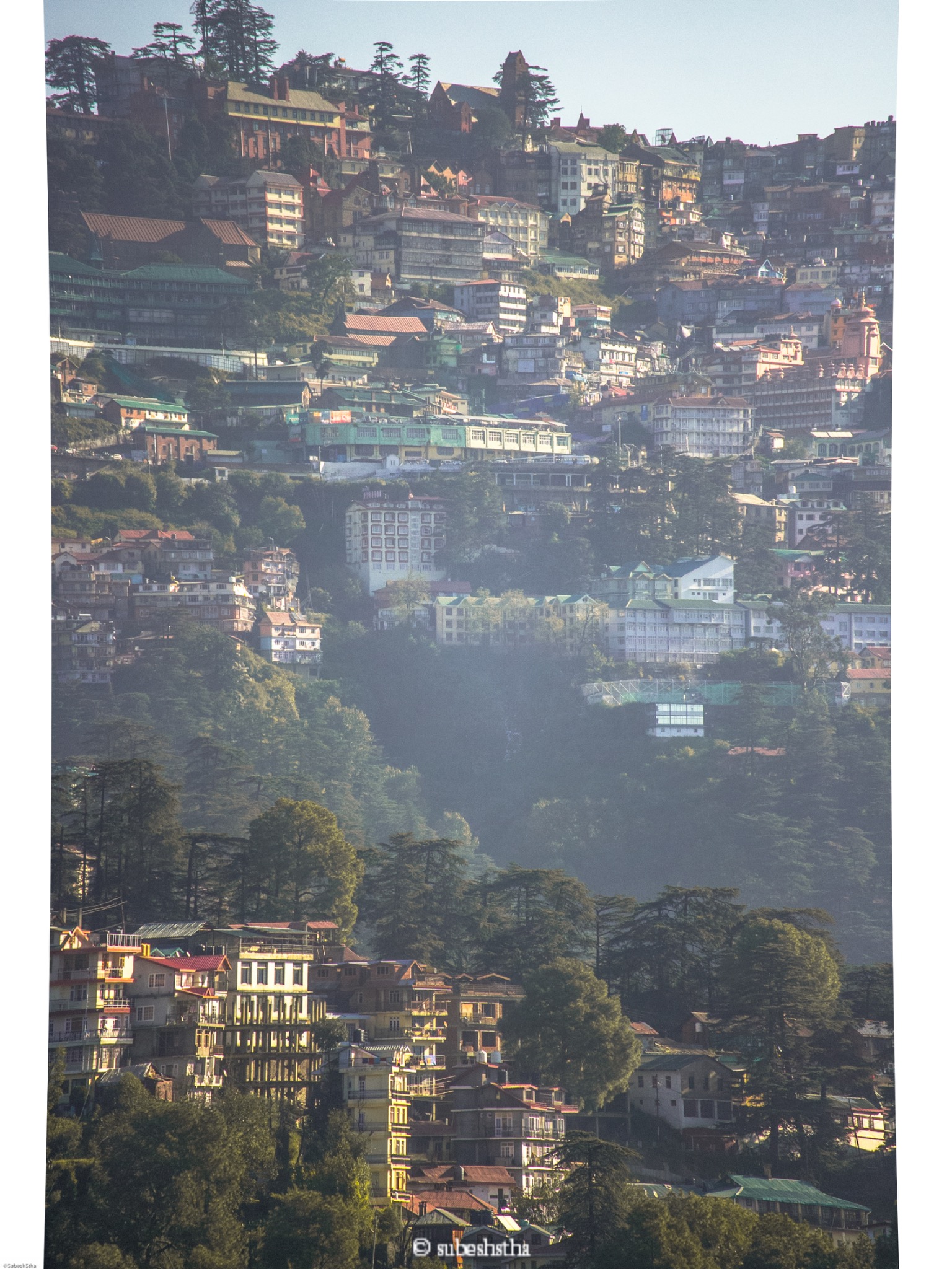 A densely built hillside settlement rising through pale mist
