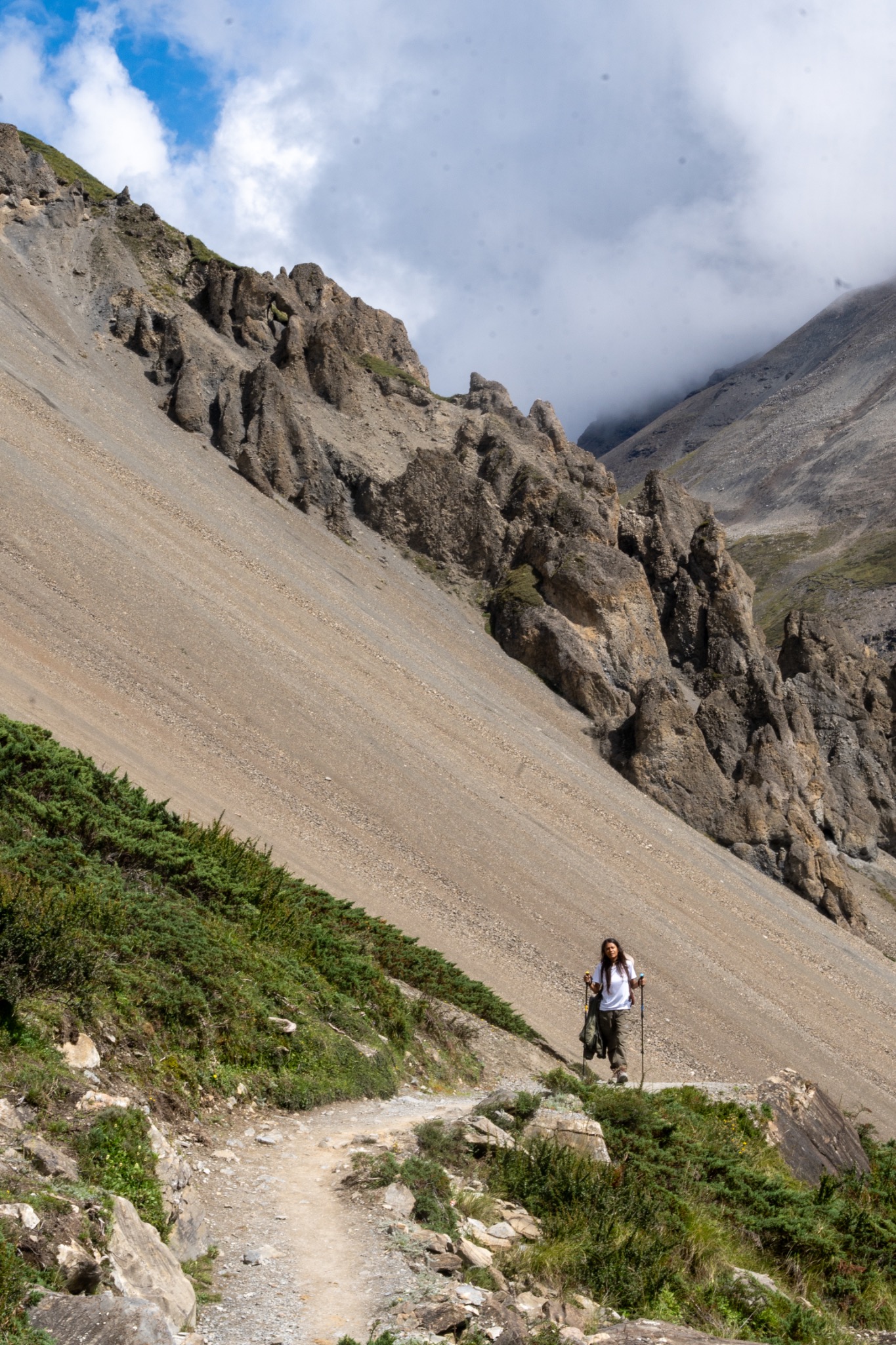 A lone hiker walking a narrow trail across a steep rocky mountainside