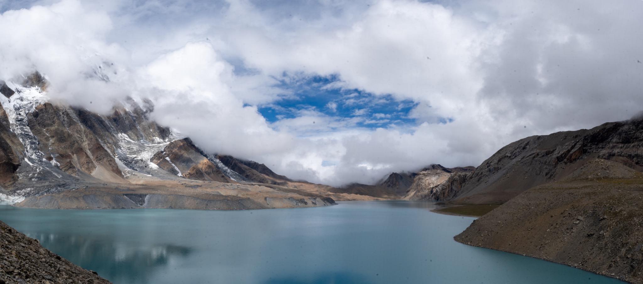 A turquoise mountain lake beneath glaciers and low clouds