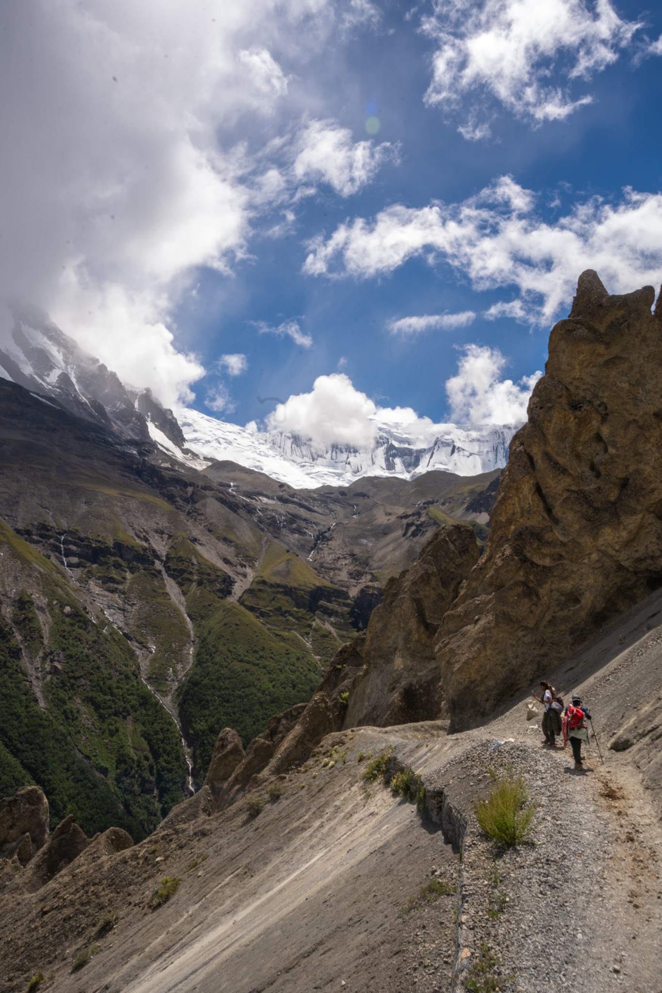 Hikers descending a narrow trail beneath snowy mountains