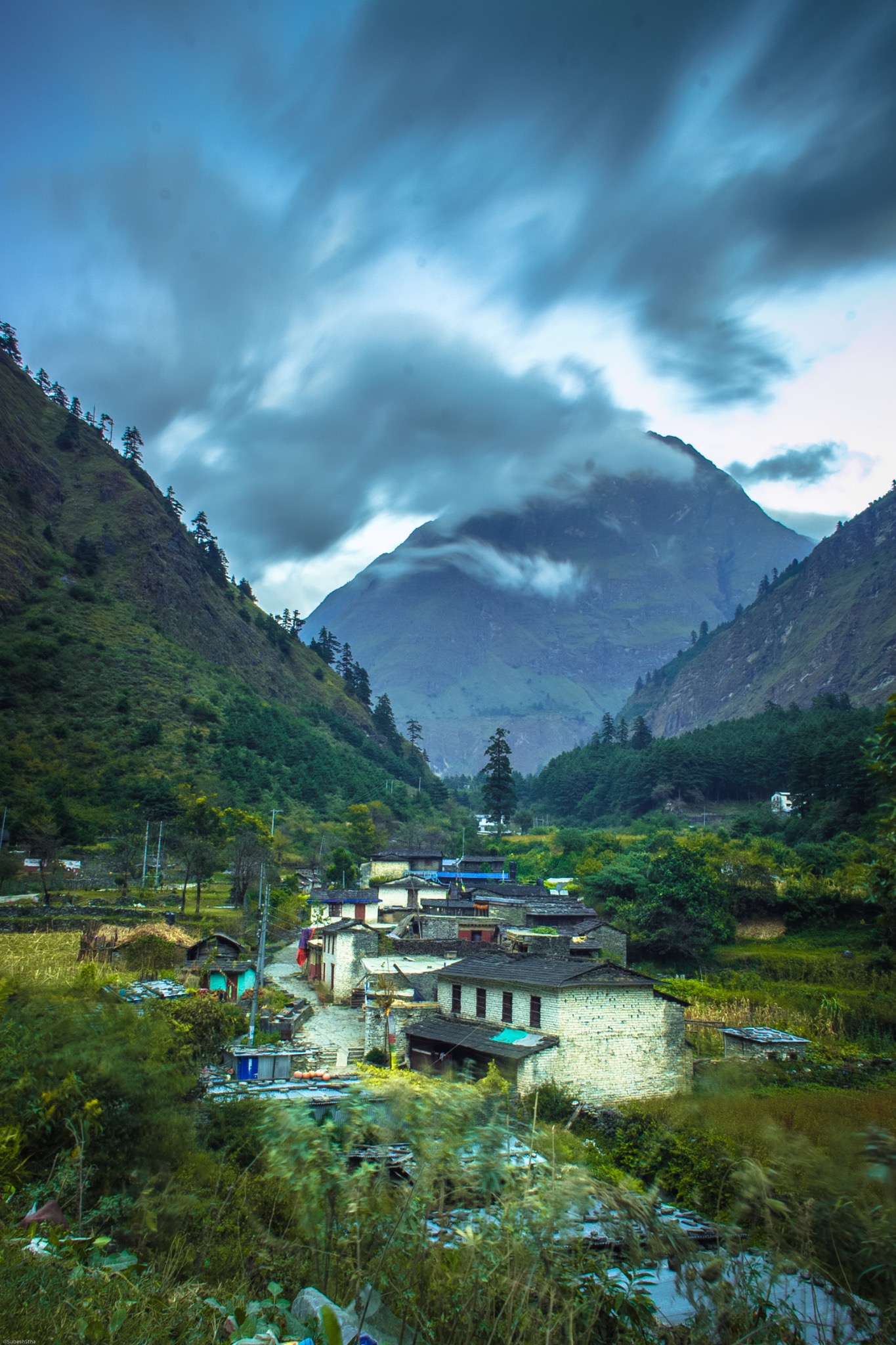 A green mountain valley beneath dramatic blue-grey clouds