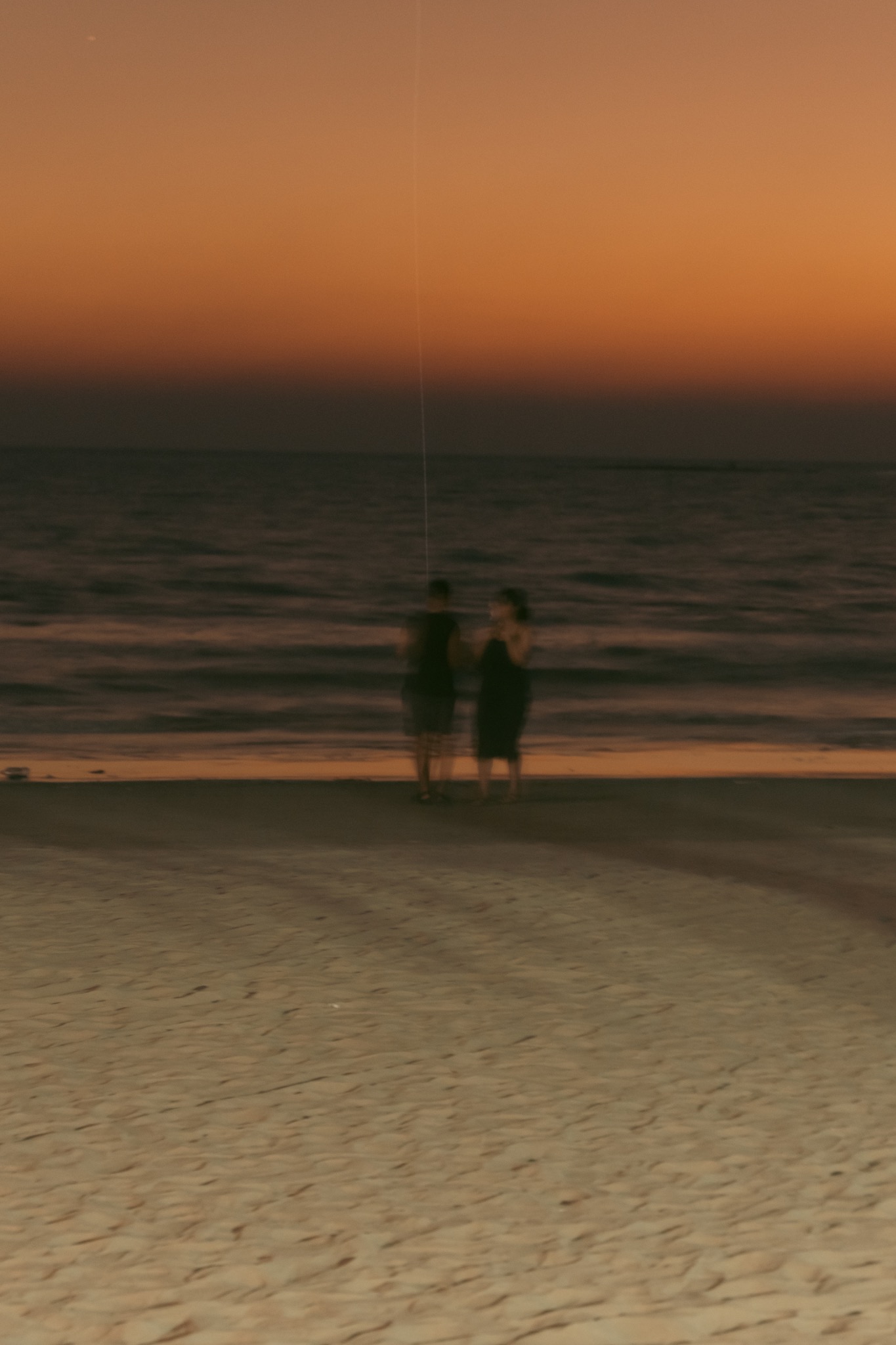 Two people standing near the sea at dusk