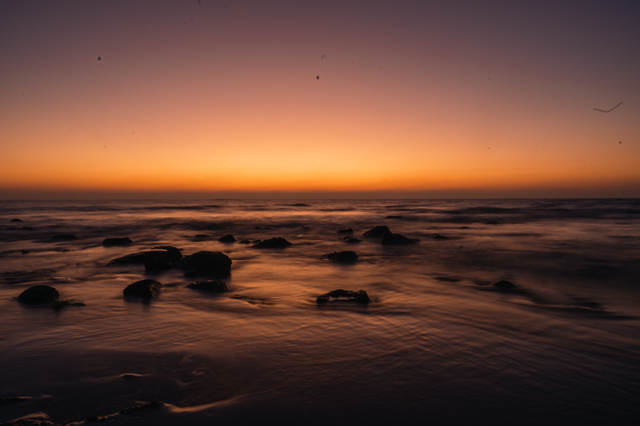 Orange dusk reflecting across a rocky shoreline and moving tide