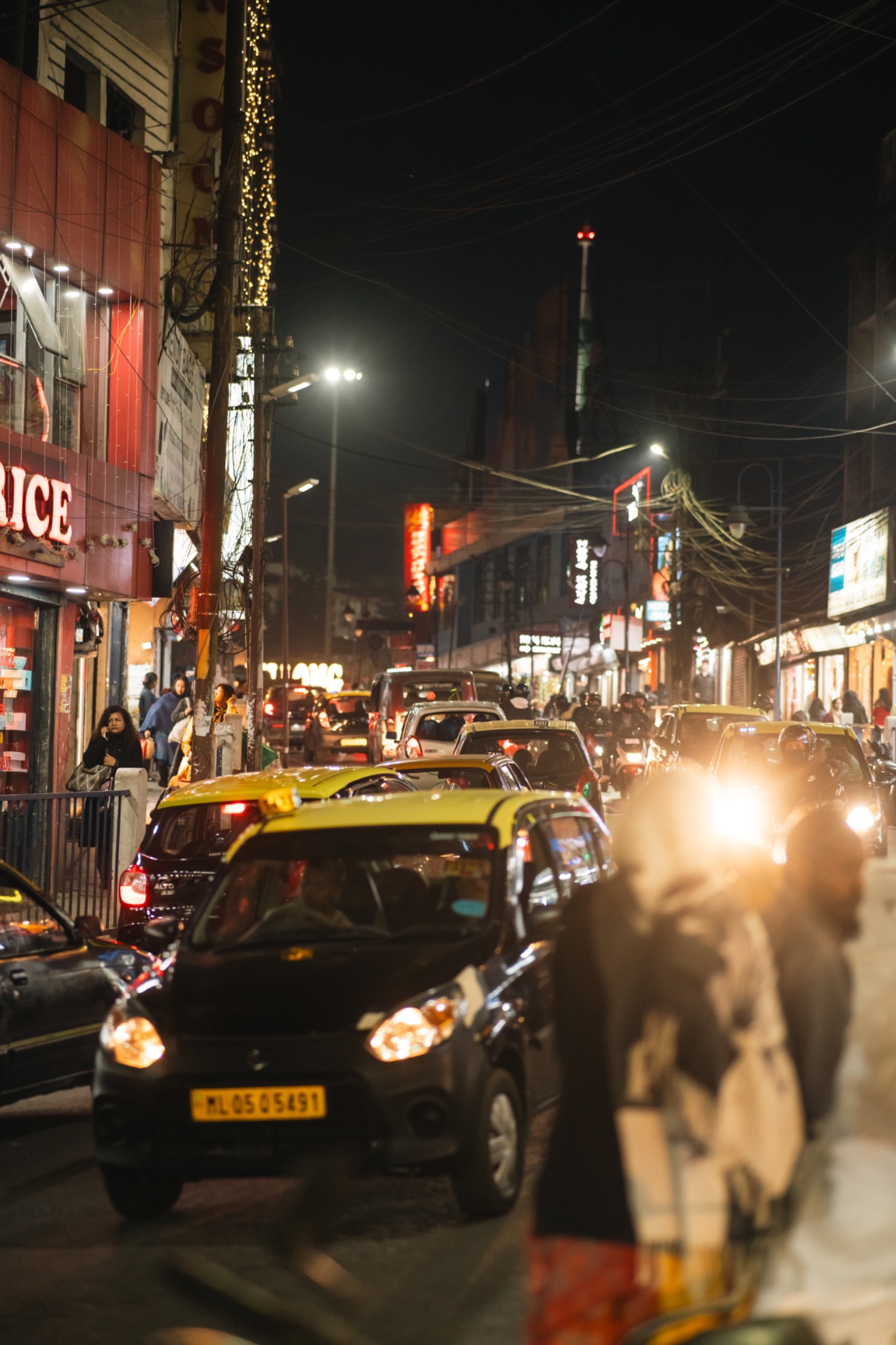 A black and yellow taxi approaching through bright night traffic